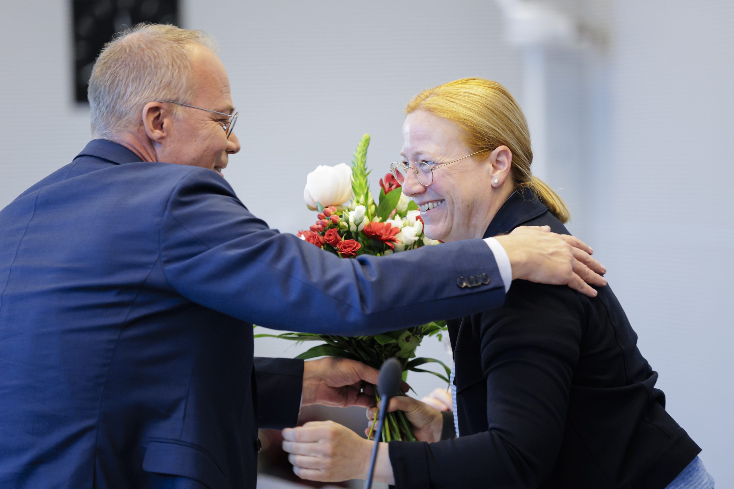 „Dagmar Schmidt lächelt herzlich, während sie einen Blumenstrauß von Matthias Miersch entgegennimmt. Beide tragen dunkle Sakkos. Miersch gratuliert ihr zur Wahl als stellvertretende Vorsitzende der SPD-Bundestagsfraktion. Die Szene zeigt eine freundliche Umarmung im Rahmen einer SPD Fraktionssitzung Bundestag.“